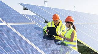 Two people in yellow hi-vis vests and orange safety helmets leaning on a solar panel in a field, 看iPad